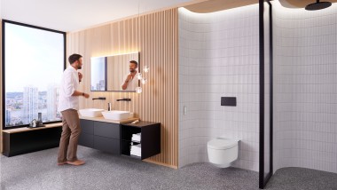 Man in bathroom standing in front of the bathroom mirror and black bathroom furniture (© Geberit)