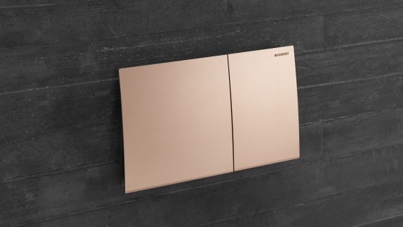 Geberit Sigma70 flush plate in red gold finish on a dark wall